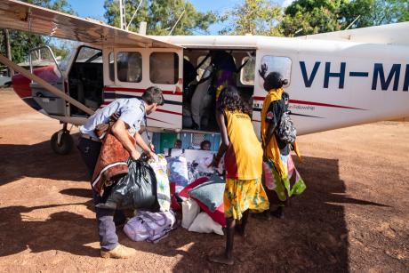 Pilot loading aircraft at airstrip with passengers standing around him