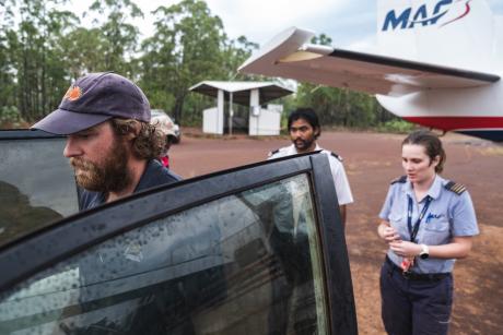 Three people standing around car in front of aircraft at airstrip