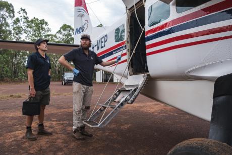 Nurses standing beisde aircraft on dirt airstrip